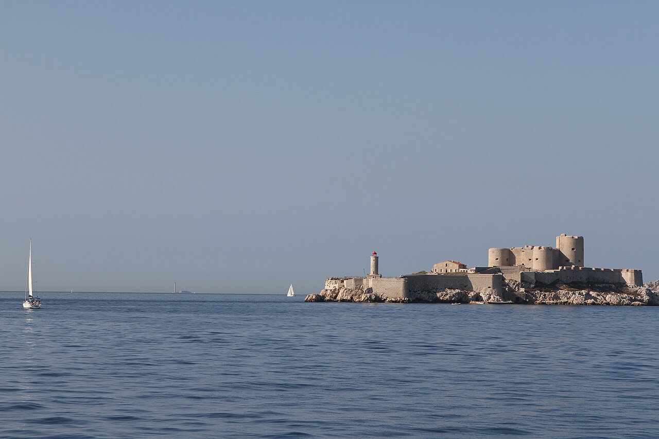 Le château d’If et son phare sur leur îlot rocheux, vus depuis un bateau, avec des voiliers au large