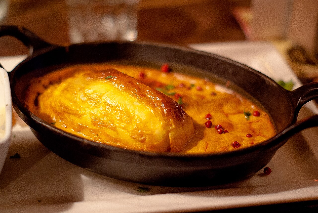Une quenelle de brochet gratinée, sauce Nantua, servie dans un plat en fonte