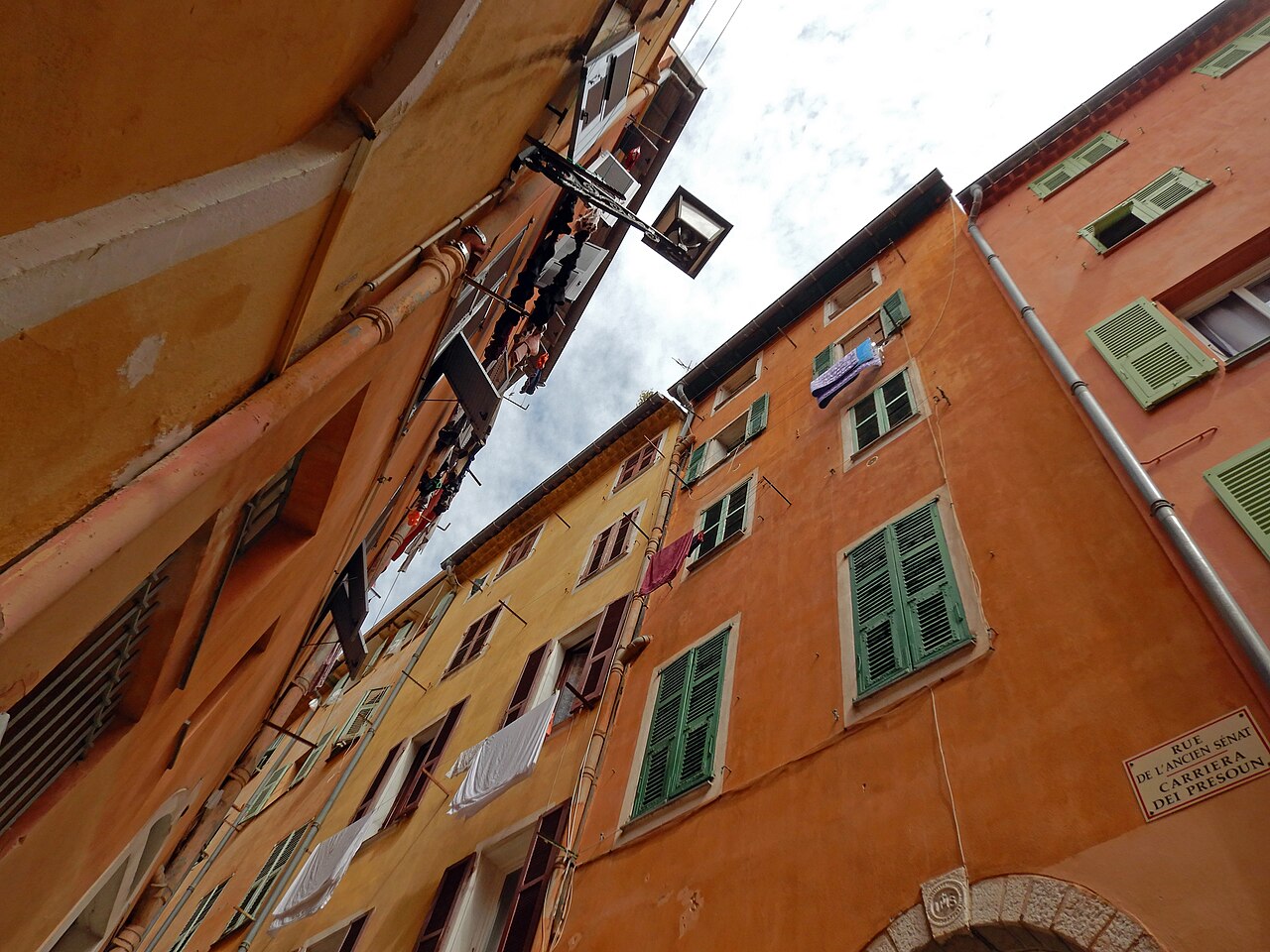 Façades ocre aux volets verts et linge aux fenêtres dans une ruelle du Vieux-Nice