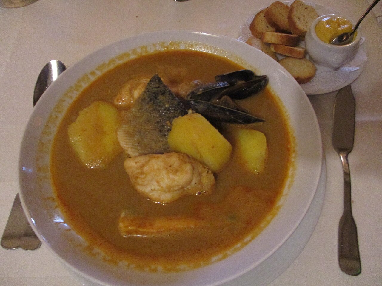 Une assiette de bouillabaisse : poissons, moules et pommes de terre dans le bouillon safrané, avec les croûtons et la rouille à côté