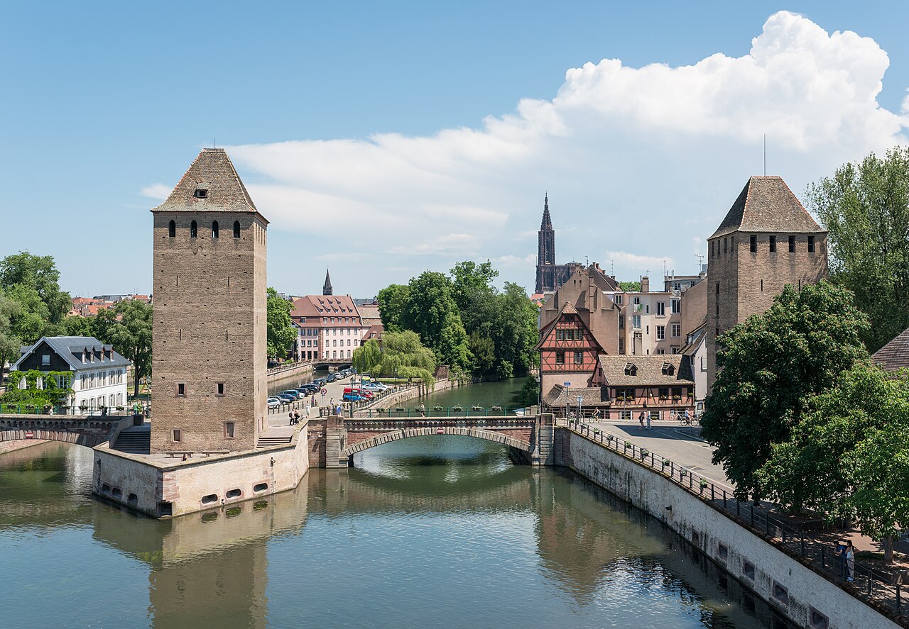 Les tours médiévales des Ponts couverts au bord de l’Ill, une maison à colombages et, au fond, la flèche de la cathédrale de Strasbourg