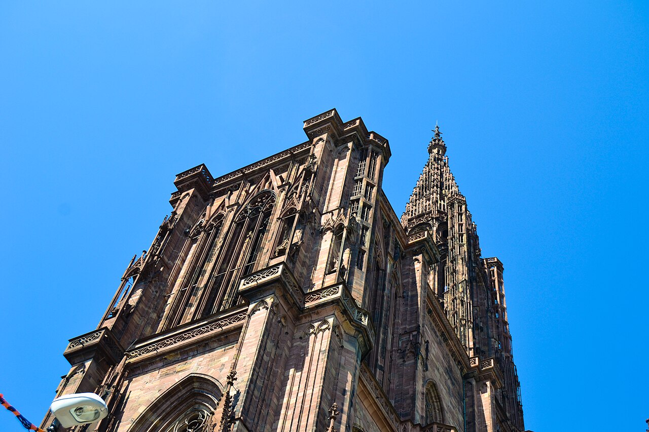 Le massif occidental en grès rose de la cathédrale de Strasbourg et sa flèche gothique, vus d’en bas sur un ciel bleu