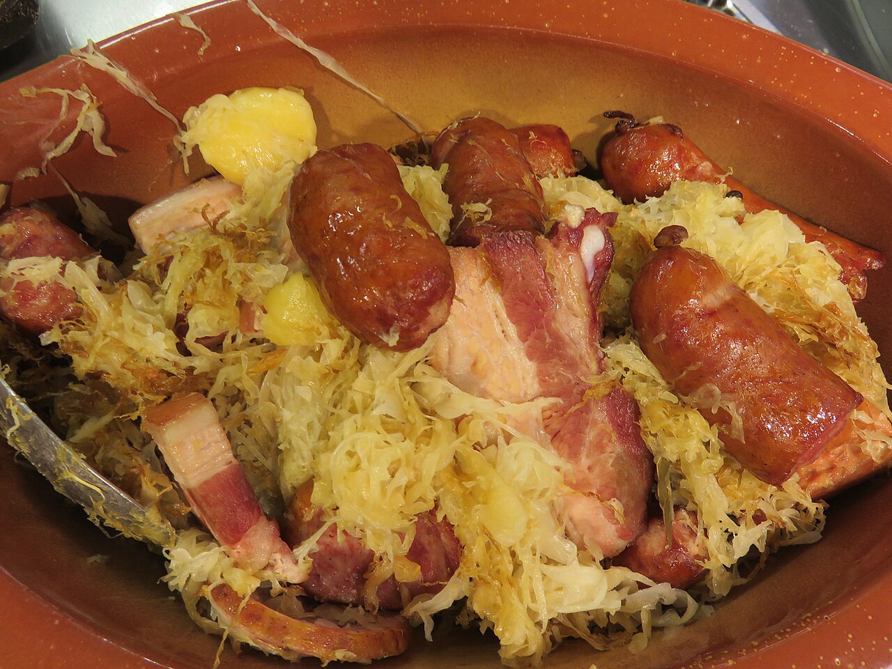 Une choucroute alsacienne garnie de saucisses, de lard et de pommes de terre dans un plat en terre cuite