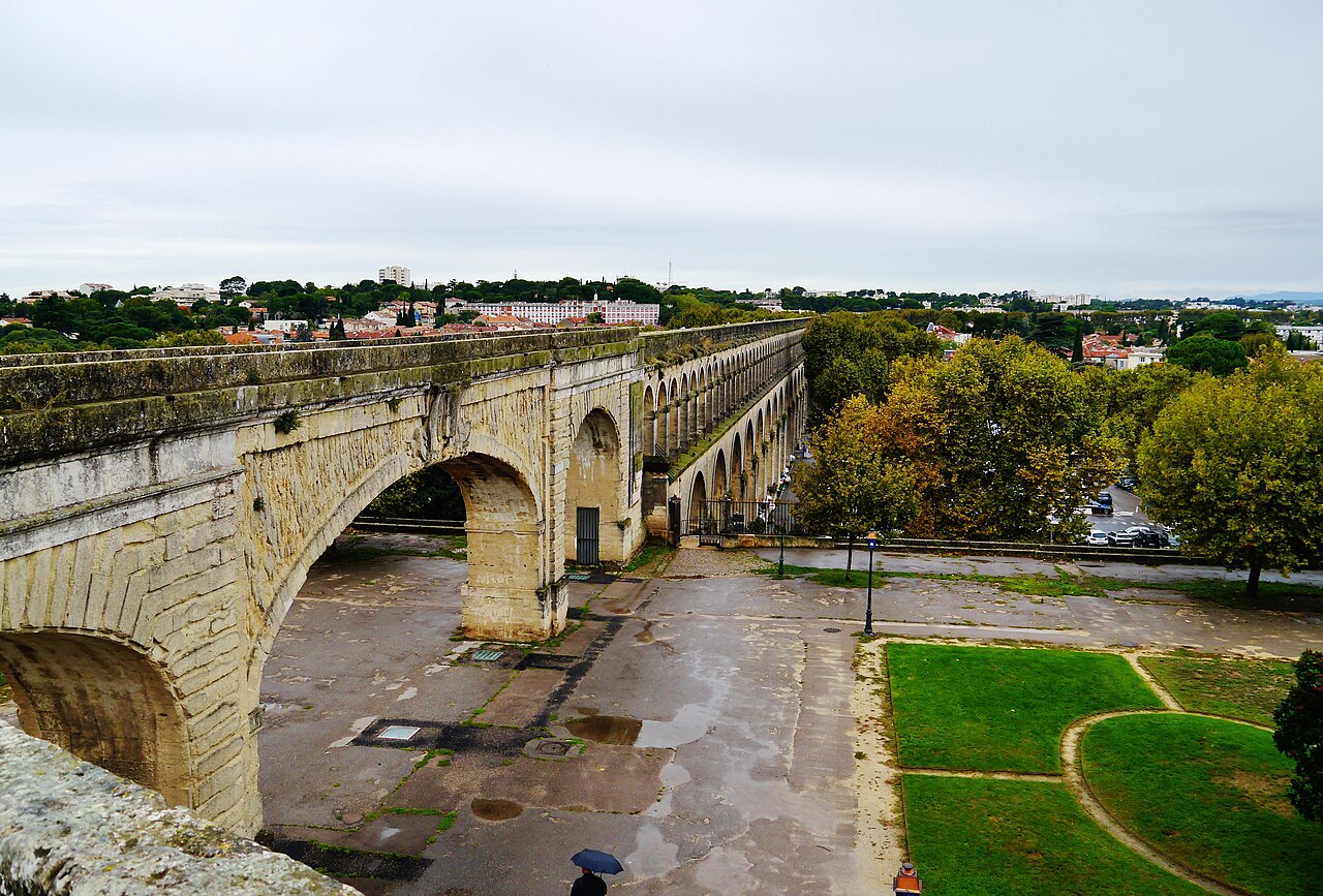 Les arches de pierre de l’aqueduc Saint-Clément vues depuis la promenade du Peyrou, au-dessus des pelouses et des arbres du quartier des Arceaux