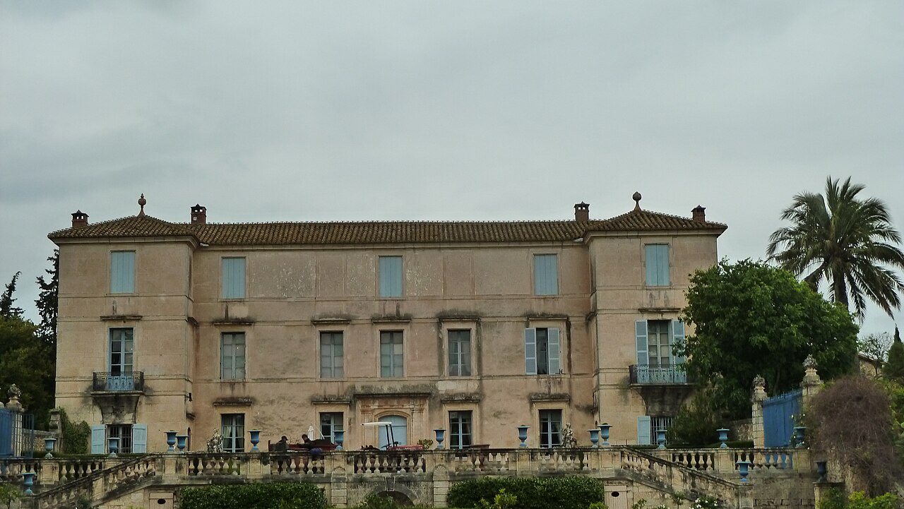 La façade du château de Flaugergues, folie montpelliéraine du XVIIIe siècle aux volets bleus, au-dessus de sa terrasse à balustres et à côté d’un grand palmier