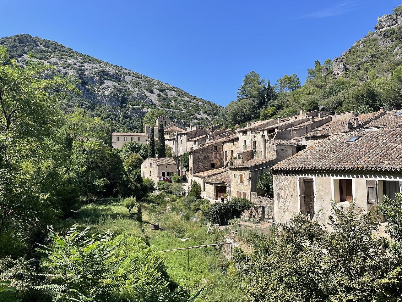 Les maisons de pierre et les toits de tuiles de Saint-Guilhem-le-Désert, le clocher de l’abbaye de Gellone et les falaises boisées du val de Gellone