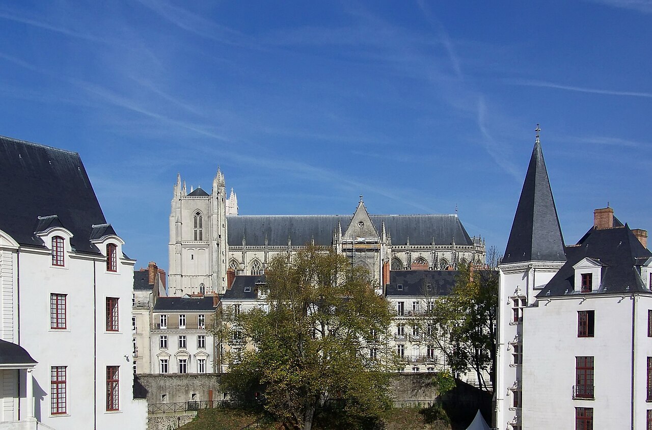La cathédrale gothique Saint-Pierre-et-Saint-Paul de Nantes, sa façade et sa longue nef, vues depuis la cour du château des ducs de Bretagne entre deux pavillons blancs