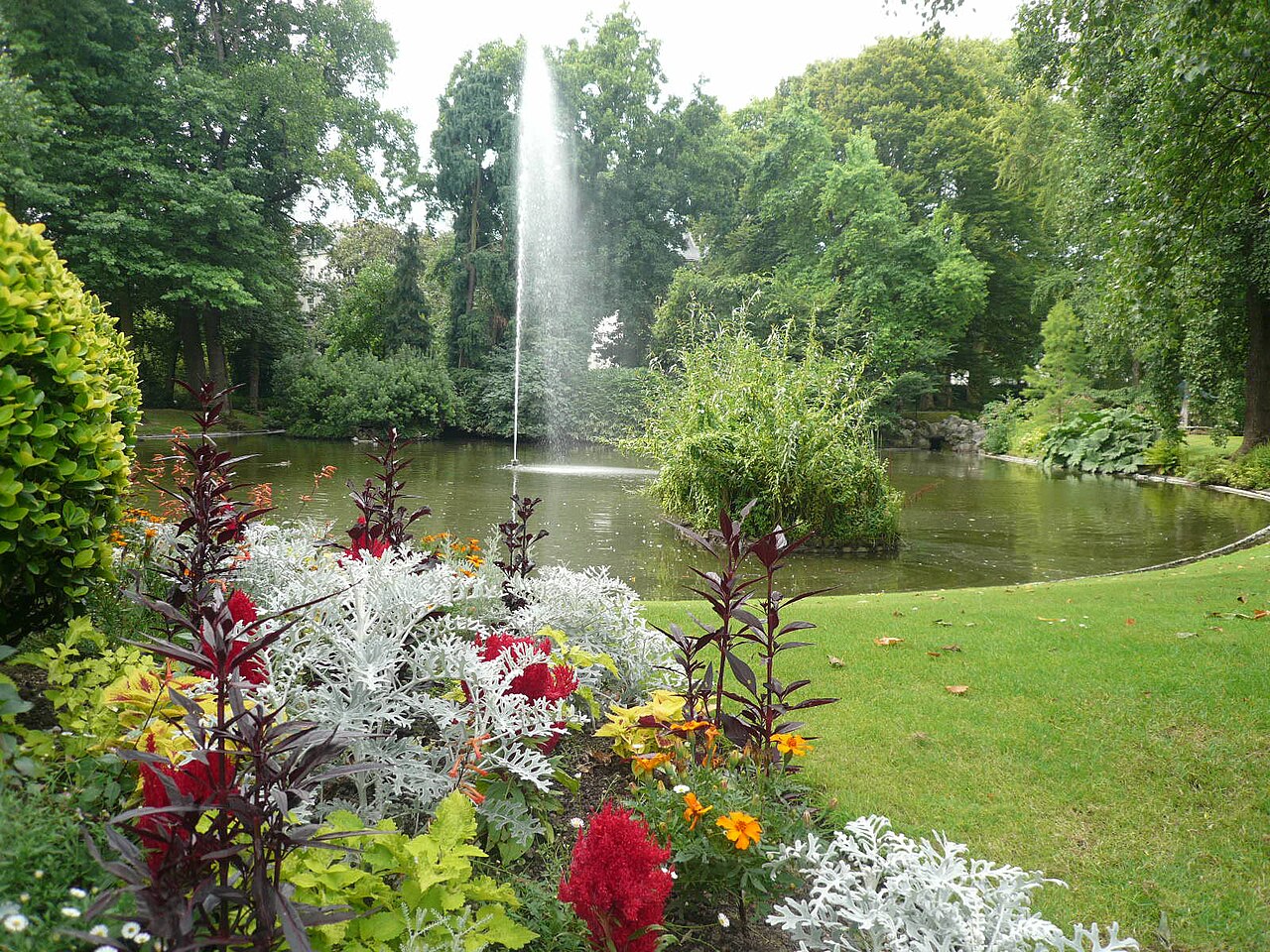 Un massif fleuri au bord du bassin du Jardin des plantes de Nantes, son jet d’eau et ses grands arbres