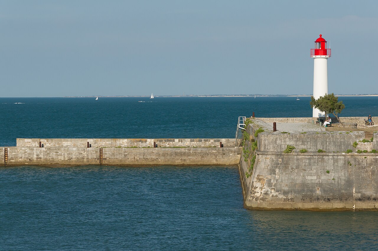 Le petit phare blanc à lanterne rouge et la jetée de pierre du port de Saint-Martin-de-Ré, devant la mer et quelques voiliers au loin