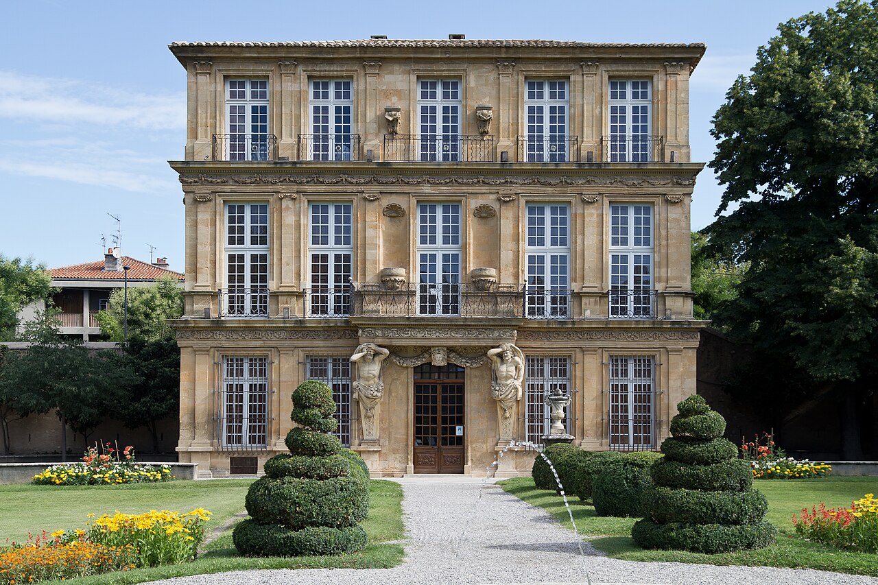 La façade du Pavillon de Vendôme à Aix-en-Provence, ses trois ordres superposés et ses atlantes encadrant la porte, devant le jardin à la française et ses buis taillés en spirale