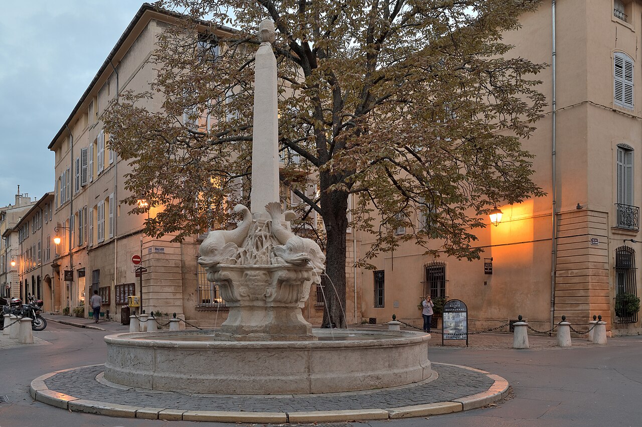 La fontaine des Quatre-Dauphins et son obélisque, au carrefour de rues bordées d’hôtels particuliers du quartier Mazarin à Aix-en-Provence, à la tombée du jour