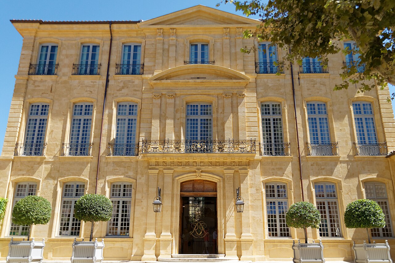 La façade sur cour de l’hôtel de Caumont à Aix-en-Provence, en pierre blonde, avec son fronton, ses balcons en fer forgé et ses orangers en caisses