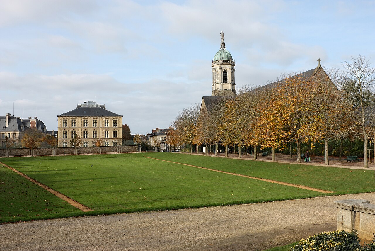 La grande pelouse du parc du Thabor en automne, bordée de marronniers dorés, devant l’église Notre-Dame-en-Saint-Melaine et son clocher surmonté d’une statue