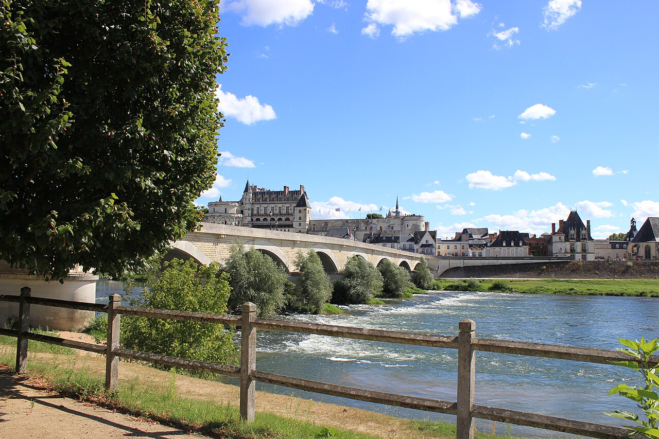 Le château royal d’Amboise dominant la Loire et le pont de pierre, vu depuis la berge et sa barrière de bois, sous un ciel d’été