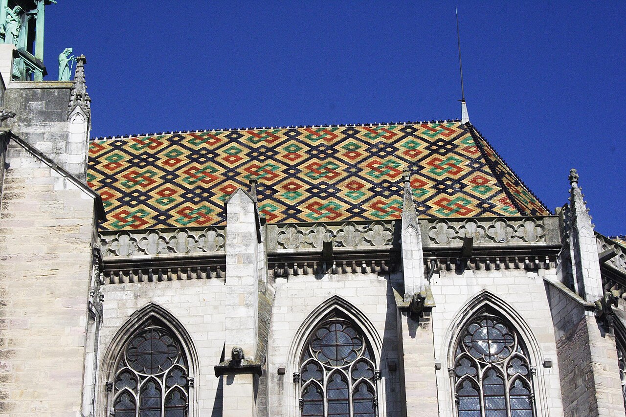 Le toit de tuiles vernissées à motifs losangés de la cathédrale Saint-Bénigne de Dijon, au-dessus de ses fenêtres gothiques, sous un ciel bleu intense
