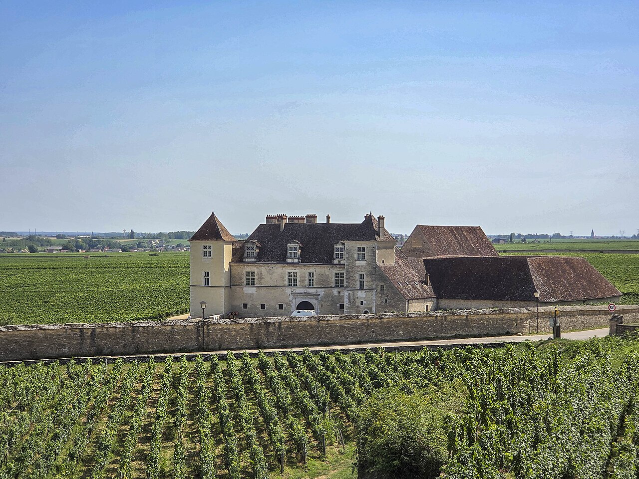 Le château du Clos de Vougeot et son mur de pierre au milieu des vignes de la Côte de Nuits, sous un ciel d’été