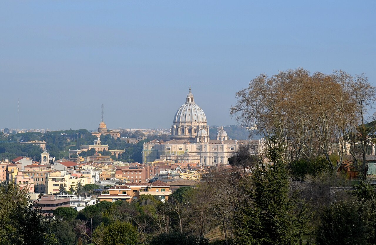 Vue de Rome depuis le Janicule : la coupole de Saint-Pierre domine les immeubles ocre du quartier et les pins, sous un ciel bleu voilé