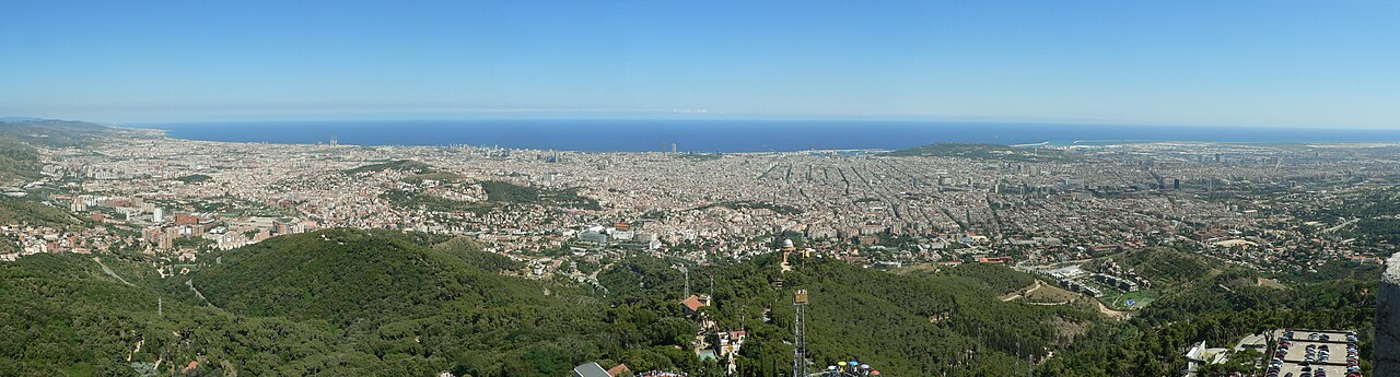 Panorama de Barcelone depuis le Tibidabo : les collines boisées au premier plan, la ville en damier jusqu’à la Méditerranée