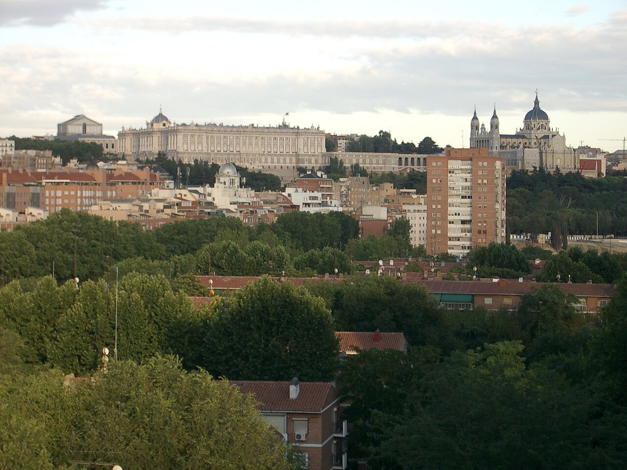 Vue générale de Madrid depuis l’ouest : le Palais royal et la cathédrale de l’Almudena dominent les toits et les immeubles de brique, au-dessus d’une masse d’arbres