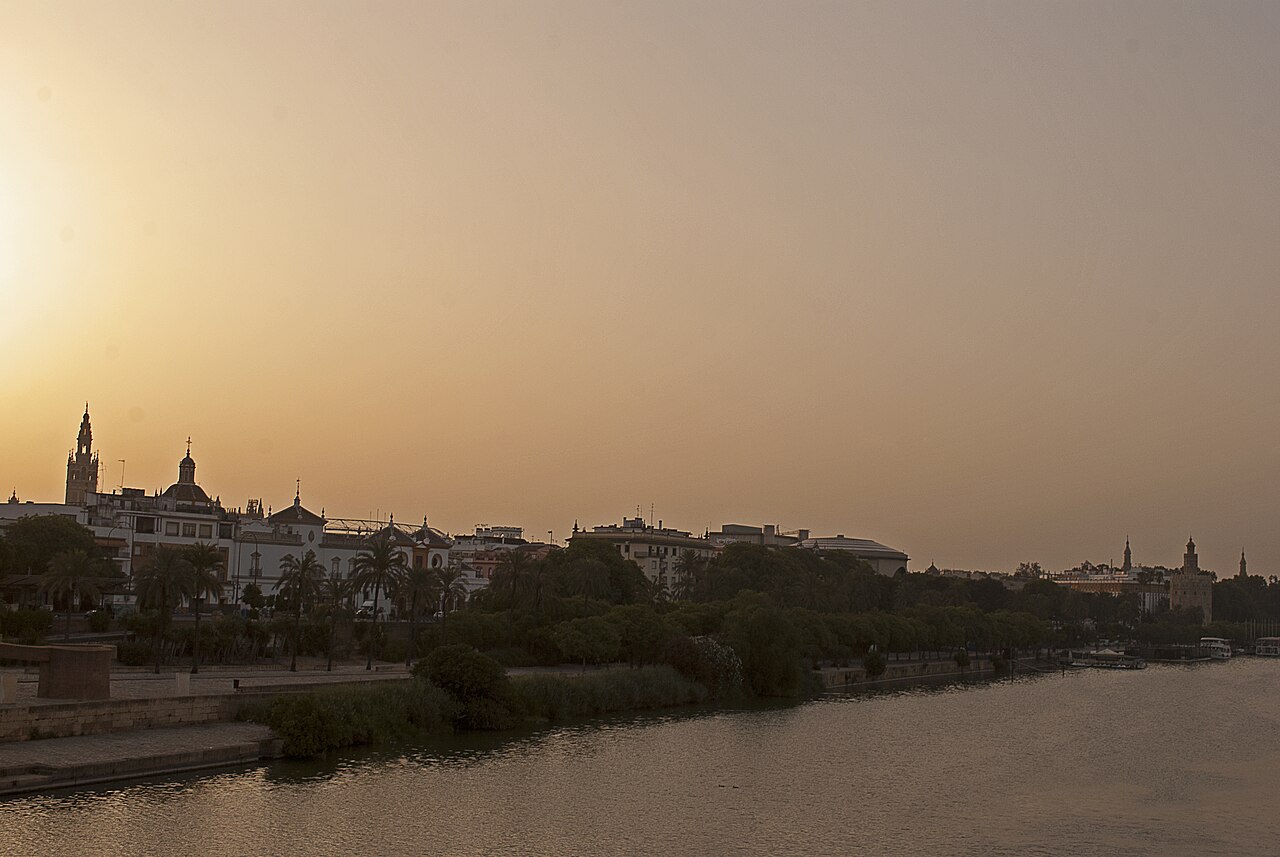 Le Guadalquivir à Séville dans la lumière dorée du soir : la Giralda et les arènes de la Maestranza à gauche, la Torre del Oro à droite, au-dessus des quais plantés de palmiers