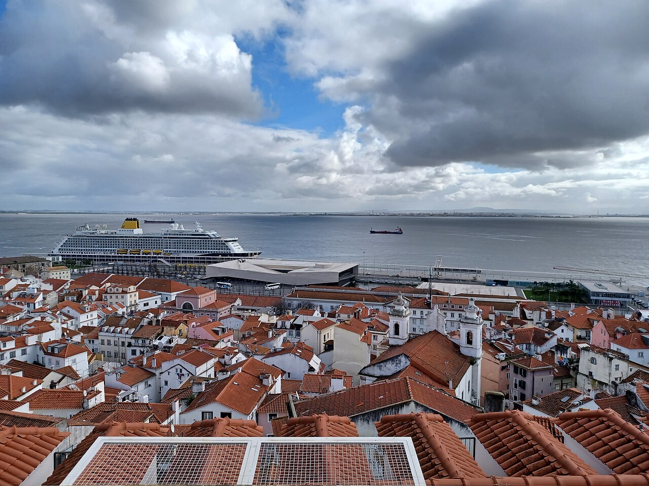 Les toits de tuiles orange de l’Alfama descendant vers le Tage, vus du belvédère de Santa Luzia à Lisbonne, un paquebot à quai et un ciel de nuages