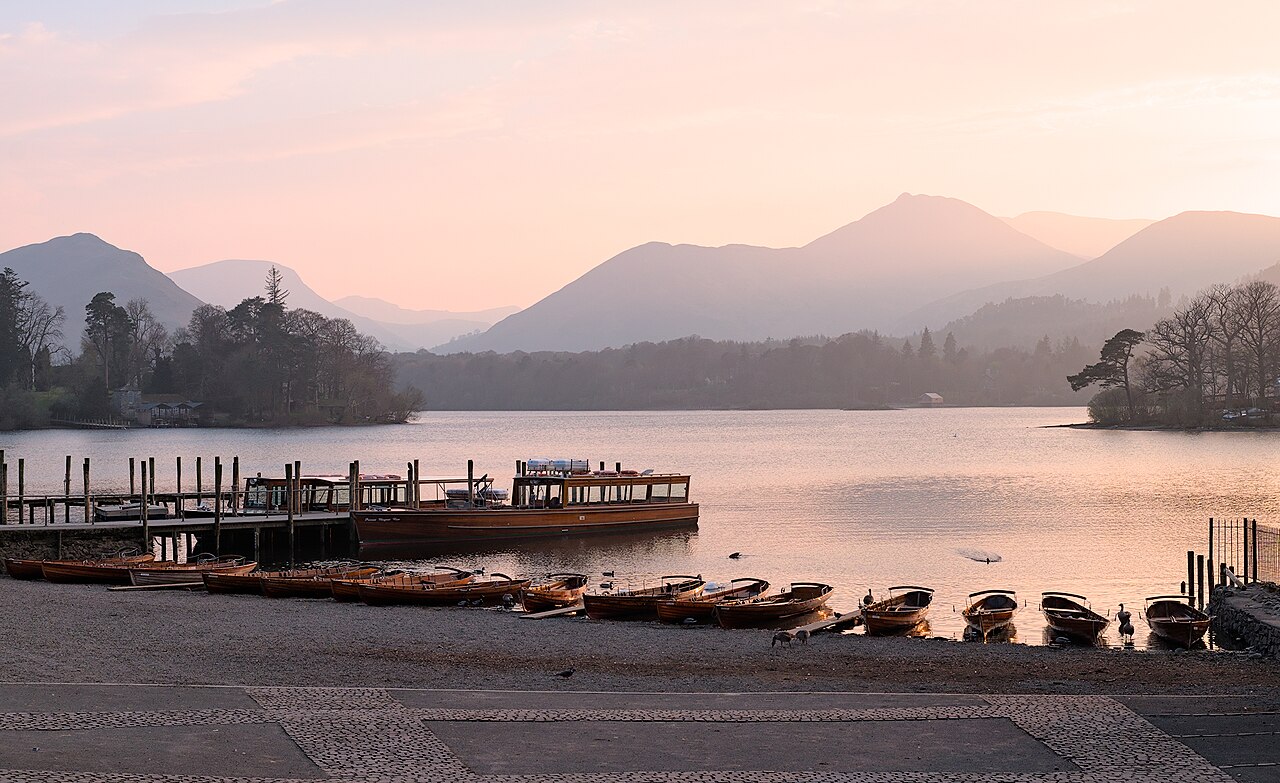 Le lac de Derwentwater, dans le Lake District, au crépuscule : barques en bois alignées sur la rive, un embarcadère et les montagnes au fond