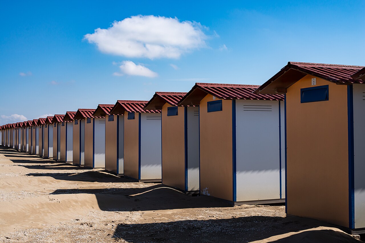 Une rangée de cabines de plage aux toits rouges sur le sable du Lido de Venise, sous un ciel bleu