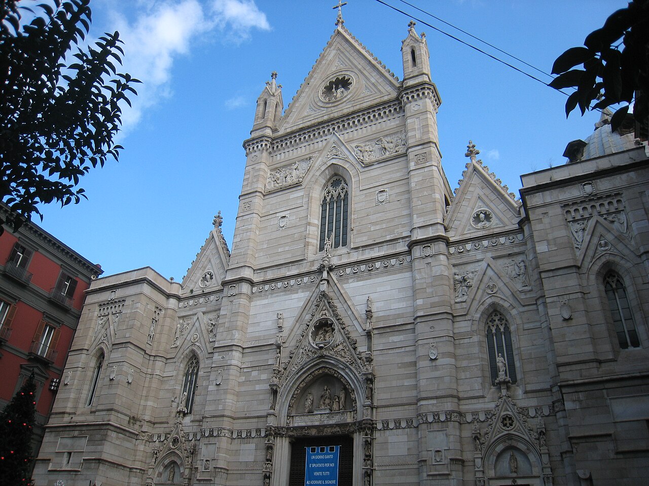 La façade néogothique de marbre blanc de la cathédrale de Naples, ses pinacles et son portail sculpté, sous un ciel bleu