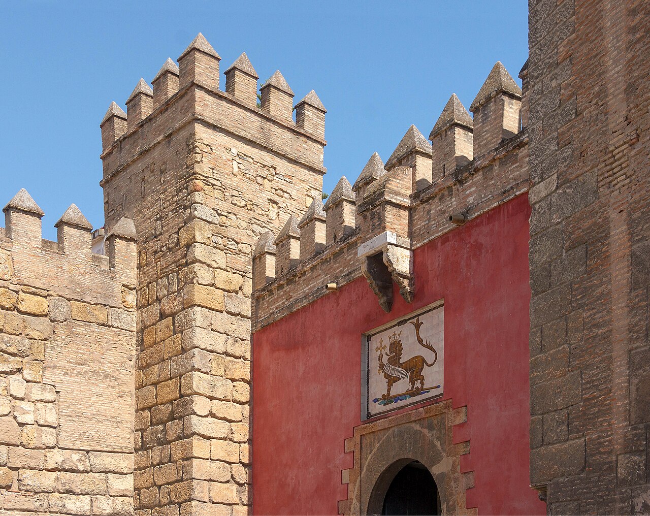 La porte du Lion du Real Alcázar de Séville : remparts crénelés et mur rouge orné d’un lion en azulejos