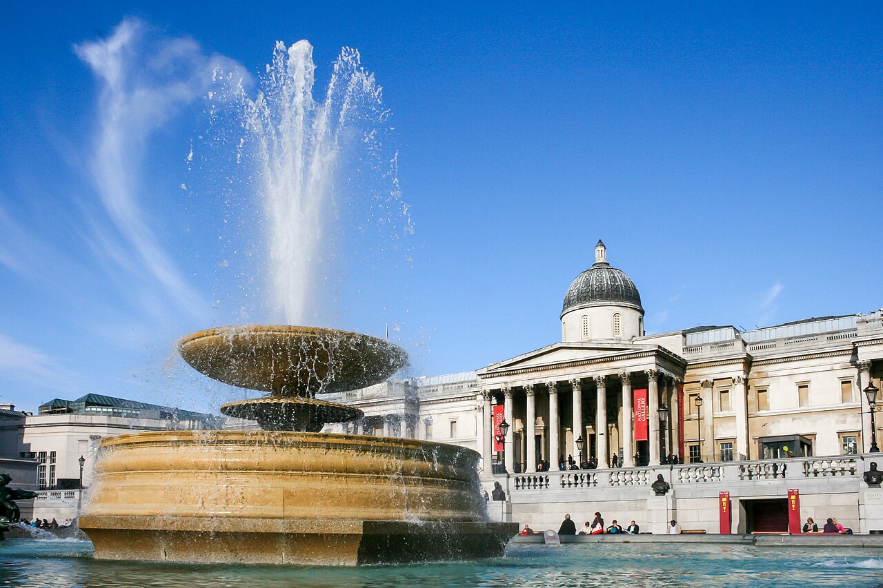 Une fontaine de Trafalgar Square en action devant la façade à colonnes et la coupole de la National Gallery
